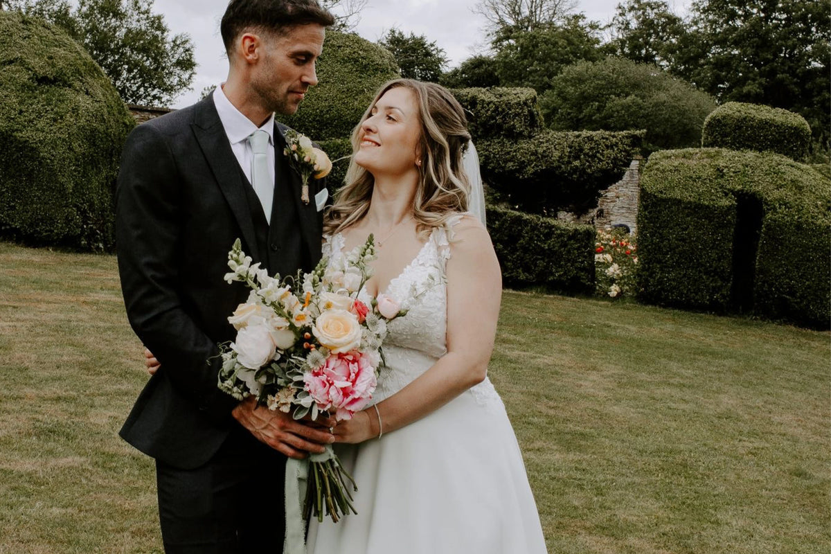 Wedding couple standing outdoors with a garden background featuring seasonal British blooms arranged by Trelowen Flowers